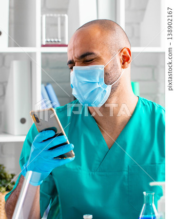 Healthcare worker checks phone while wearing mask and gloves in medical setting Healthcare worker checks phone while wearing mask and gloves in medical setting 138902167