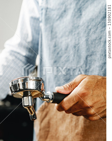Coffee preparation involves a person holding a portafilter in a cafe setting Coffee preparation involves a person holding a portafilter in a cafe setting 138902181