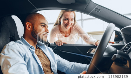 Man sits in car while woman talks to him inside a vehicle showroom 138902189