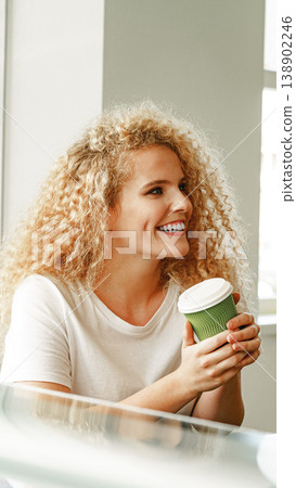 Woman holds a green cup while sitting in a bright cafe during the day 138902246