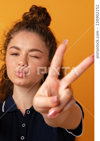 Young person making peace sign and kissy face in front of bright orange background Young person making peace sign and kissy face in front of bright orange background 138902252