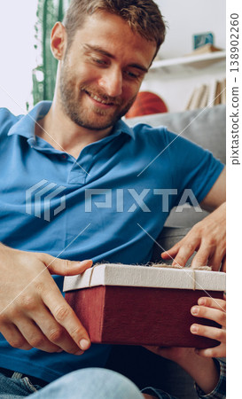 Father and child open a gift together in their living room on a sunny day Father and child open a gift together in their living room on a sunny day 138902260