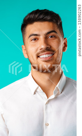 Young man smiles against a bright blue background in a casual setting inside a studio Young man smiles against a bright blue background in a casual setting inside a studio 138902263