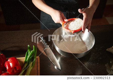Hands Sifting Flour Into Mixing Bowl on Kitchen Counter With Knife and Fresh Vegetables Hands Sifting Flour Into Mixing Bowl on Kitchen Counter With Knife and Fresh Vegetables 138902313