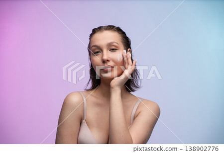 Young woman applying face cream on her cheek, promoting a daily beauty routine for healthy skin on a colorful background with copy space, focusing on skincare and hydration Young woman applying face cream on her cheek, promoting a daily beauty routine for healthy skin on a colorful background with copy space, focusing on skincare and hydration 138902776