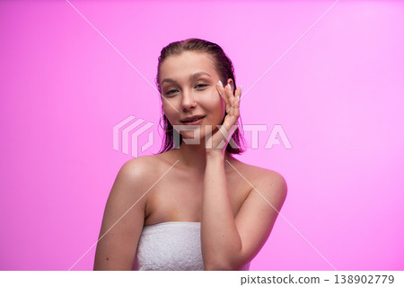 Young woman applying nourishing face cream for hydrated, clean skin on a pink background, embracing a healthy beauty routine and self-care for wellness Young woman applying nourishing face cream for hydrated, clean skin on a pink background, embracing a healthy beauty routine and self-care for wellness 138902779