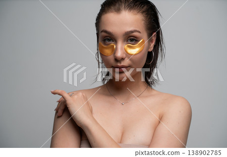 Woman with wet hair applying gold hydrogel eye patches for under eye treatment, focusing on facial skin care, beauty routines, and well-being at home Woman with wet hair applying gold hydrogel eye patches for under eye treatment, focusing on facial skin care, beauty routines, and well-being at home 138902785