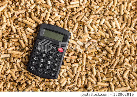 Calculator and Wood Pellets Representing Biomass Fuel Cost, Renewable Energy Budget and Home Heating Expenses Calculator and Wood Pellets Representing Biomass Fuel Cost, Renewable Energy Budget and Home Heating Expenses 138902919