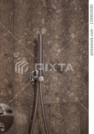 Modern chrome showerhead installed on textured stone wall in contemporary bathroom setting 138903080
