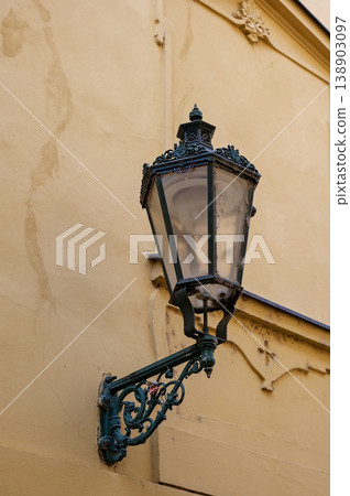 Vintage street lamp mounted on yellow wall with intricate design and glass enclosure Vintage street lamp mounted on yellow wall with intricate design and glass enclosure 138903097