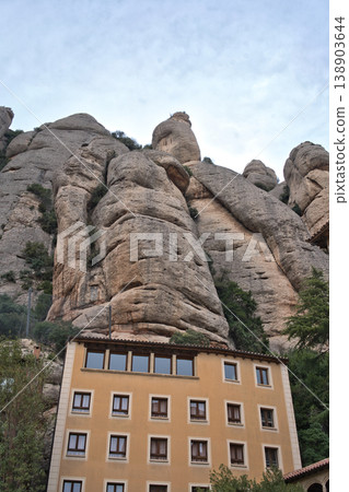 A building nestled at the base of the dramatic, weathered rock formations of Montserrat mountain in Catalonia, Spain A building nestled at the base of the dramatic, weathered rock formations of Montserrat mountain in Catalonia, Spain 138903644