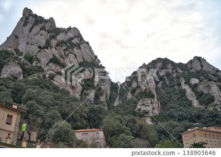 Dramatic rock formations of Montserrat mountain range in Catalonia, Spain, with lush green vegetation and buildings nestled below Dramatic rock formations of Montserrat mountain range in Catalonia, Spain, with lush green vegetation and buildings nestled below 138903646