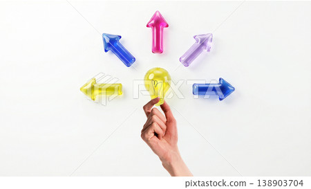 Hand holding light bulb among arrows symbolizing idea selection and innovation direction. 138903704