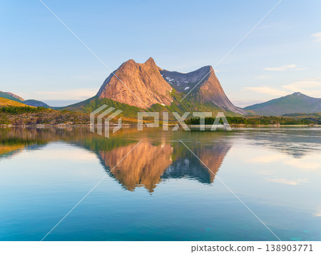 Mountain peaks reflecting in the calm fjord water during midnight sun in Norway. 138903771