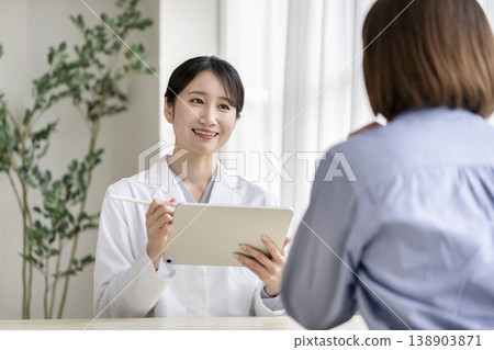 A smiling female doctor conducts a medical interview while holding a tablet. A smiling female doctor conducts a medical interview while holding a tablet. 138903871