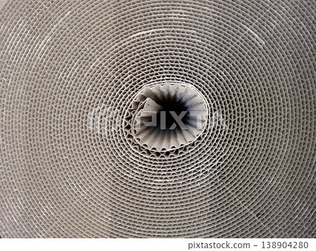A large roll of corrugated cardboard sits on a workshop floor. The top view reveals a spiral texture that is both unique and detailed. The light highlights the grooves and patterns in the material. 138904280