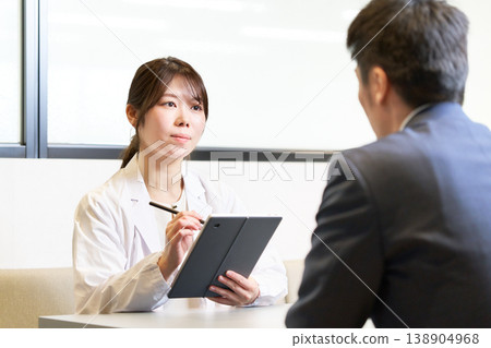 一位女性工業醫學專家手持平板電腦,認真傾聽一位員工的敘述。 一位女性工業醫學專家手持平板電腦,認真傾聽一位員工的敘述。 138904968