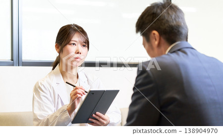 一位女性工業醫學專家手持平板電腦，認真傾聽一位員工的敘述。 138904970