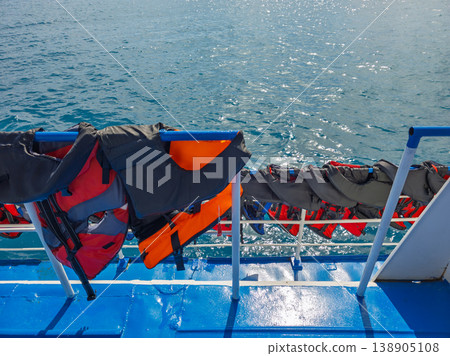 Life vests hanging on boat deck with blue water reflection Life vests hanging on boat deck with blue water reflection 138905108