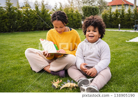Children reading book with dinosaur toys in backyard Children reading book with dinosaur toys in backyard 138905190
