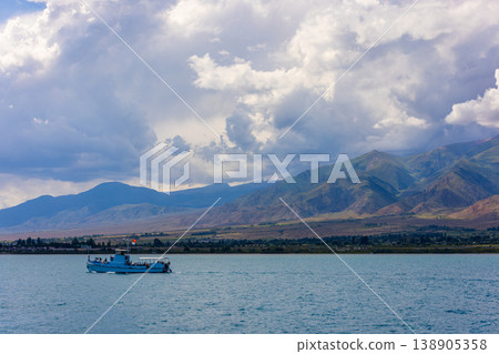Blue passenger boat on serene Issyk-Kul lake with mountains in background Blue passenger boat on serene Issyk-Kul lake with mountains in background 138905358