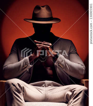 Stylish, fashionable and trendy man in silhouette sitting in a dark room with a red studio background. Edgy, mysterious and curious male mafia boss sitting in a fancy suit, hat and expensive jewelry Stylish, fashionable and trendy man in silhouette sitting in a dark room with a red studio background. Edgy, mysterious and curious male mafia boss sitting in a fancy suit, hat and expensive jewelry 138905901