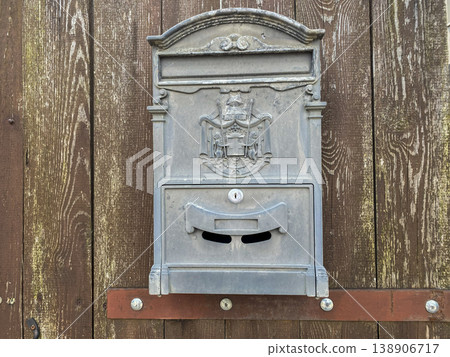 Old metal mailbox mounted on wooden wall in a rural setting with a historical design 138906717