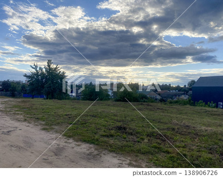 Clouds gather over a small village on a sunny evening in summer near a grassy hillside 138906726