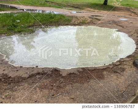 Water collects in large puddle on dirt path near grassy area in public park 138906787