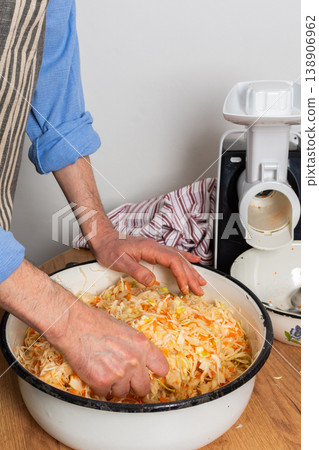 A 53-year-old man works in his kitchen mixing chopped cabbage and grated carrots in a bowl. He prepares to ferment the vegetables for preservation and flavor 138906962