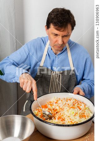 A 53-year-old man mixes cabbage and carrots in a large bowl in his kitchen while preparing for fermentation using simple tools and ingredients A 53-year-old man mixes cabbage and carrots in a large bowl in his kitchen while preparing for fermentation using simple tools and ingredients 138906963