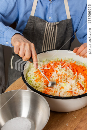 A 53-year-old man mixes cabbage and carrots in a large bowl in his kitchen while preparing for fermentation using simple tools and ingredients A 53-year-old man mixes cabbage and carrots in a large bowl in his kitchen while preparing for fermentation using simple tools and ingredients 138906966