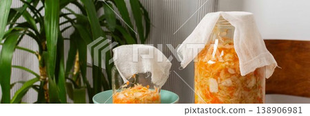 Jars containing cabbage and carrots are fermenting on a wooden table. Cloth covers the jars to allow air while keeping dust out. This is part of food preparation at home, banner Jars containing cabbage and carrots are fermenting on a wooden table. Cloth covers the jars to allow air while keeping dust out. This is part of food preparation at home, banner 138906981