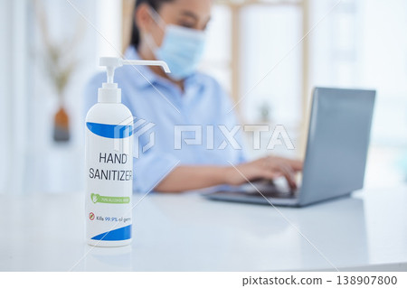 Hand sanitizer, covid and business woman typing on a laptop at desk in her office with face mask. Hygiene, technology and professional employee working on project with computer during corona pandemic Hand sanitizer, covid and business woman typing on a laptop at desk in her office with face mask. Hygiene, technology and professional employee working on project with computer during corona pandemic 138907800