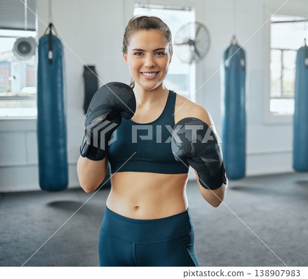 Boxing, fighting and gloves with a female boxer standing in a health club or sports gym. Portrait of a strong and tough young woman training, exercising and practicing self defense during a workout 138907983
