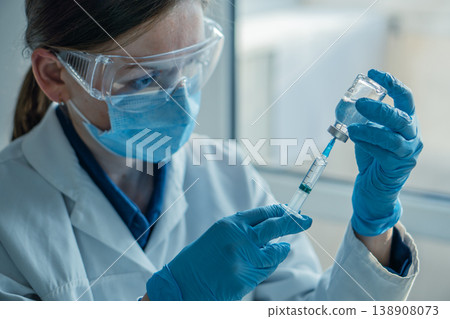 A professional nurse wearing gloves and safety gear prepares a vaccine dose in a clinical setting. The image highlights modern healthcare, vaccination, and disease prevention efforts A professional nurse wearing gloves and safety gear prepares a vaccine dose in a clinical setting. The image highlights modern healthcare, vaccination, and disease prevention efforts 138908073