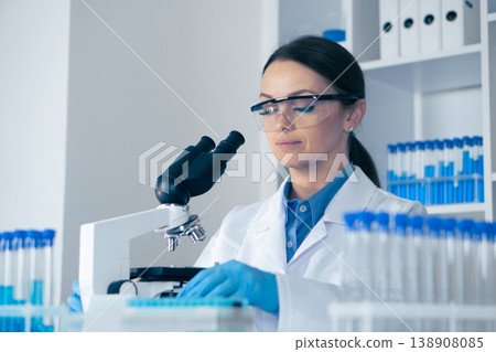 In a wellequipped lab, a dedicated female scientist in a white coat examines samples under a microscope, surrounded by colorful test tubes, showcasing her commitment to biology and chemistry In a wellequipped lab, a dedicated female scientist in a white coat examines samples under a microscope, surrounded by colorful test tubes, showcasing her commitment to biology and chemistry 138908085