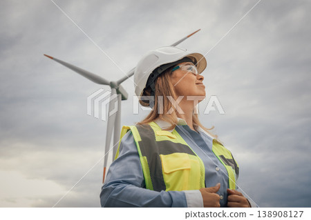A highly skilled female engineer, dressed in safety gear, stands confidently before a towering wind turbine, which symbolizes both progress and innovation in the vital field of renewable energy A highly skilled female engineer, dressed in safety gear, stands confidently before a towering wind turbine, which symbolizes both progress and innovation in the vital field of renewable energy 138908127