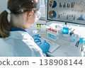 A woman scientist works at a computer, examining scientific data visualizations and laboratory test results. The scene highlights innovation, research, and technology in a bright, modern lab setting 138908144