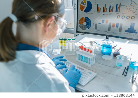 A woman scientist works at a computer, examining scientific data visualizations and laboratory test results. The scene highlights innovation, research, and technology in a bright, modern lab setting A woman scientist works at a computer, examining scientific data visualizations and laboratory test results. The scene highlights innovation, research, and technology in a bright, modern lab setting 138908144