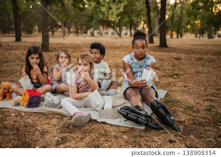 Children watching a movie in the park eating snacks from paper bags 138908354