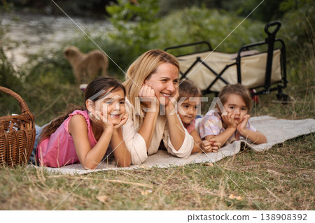 Happy mother and daughters enjoying a picnic in a park Happy mother and daughters enjoying a picnic in a park 138908392