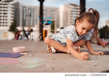Little girl drawing with chalks on the pavement in a playground Little girl drawing with chalks on the pavement in a playground 138908434