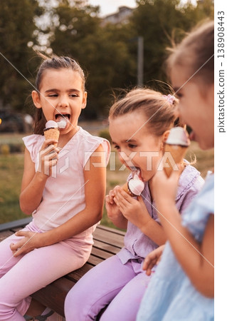 Three little girls enjoying ice cream cones in a park 138908443