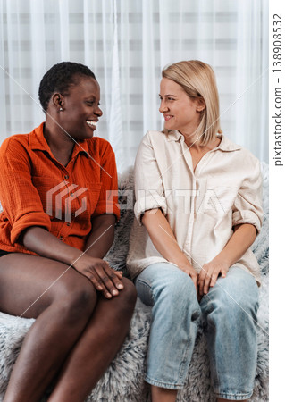 Two young women smiling and talking, sitting on a sofa Two young women smiling and talking, sitting on a sofa 138908532