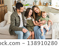 Happy family at home. Mother father two children daughters relaxing on sofa indoor. Mom dad parents baby girls kids relax playing having fun together. Family smiling laughing enjoying tender moment 138910280