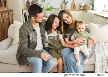 Happy family at home. Mother father two children daughters relaxing on sofa indoor. Mom dad parents baby girls kids relax playing having fun together. Family smiling laughing enjoying tender moment 138910280