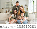 Happy family at home. Mother father two children daughters relaxing on sofa indoor. Mom dad parents baby girls kids relax playing having fun together. Family smiling laughing enjoying tender moment 138910281