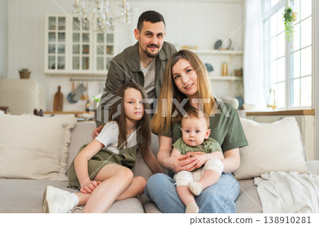 Happy family at home. Mother father two children daughters relaxing on sofa indoor. Mom dad parents baby girls kids relax playing having fun together. Family smiling laughing enjoying tender moment 138910281
