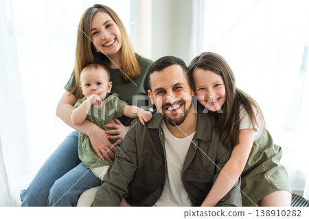 Happy family at home. Mother father two children daughters relaxing indoor. Mom dad parents baby girls kids relax playing having fun together. Family smiling laughing enjoying tender love moment 138910282